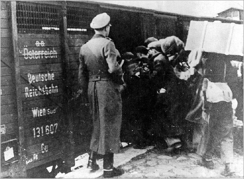 A German officer overseeing Jews from Vienna who hold their belongings as they board a railroad freight car